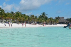 A beach with clear turquoise water, palm trees, and a thatched-roof building. - Beautiful Studio In Akumal, Half Moon Bay - Wifi, AC (Akumal, Riviera Maya)