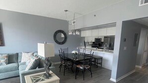 A modern living room with a sofa, coffee table, and dining area with chairs and a chandelier. - NEWLY TOTALLY RENOVATED   5⭐️STAR sleeps 8  (Panama City Beach)