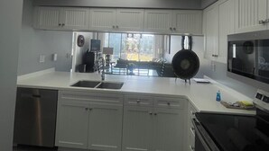 A modern kitchen with white cabinetry, a stainless steel dishwasher, and a large island with a sink. - NEWLY TOTALLY RENOVATED   5⭐️STAR sleeps 8  (Panama City Beach)
