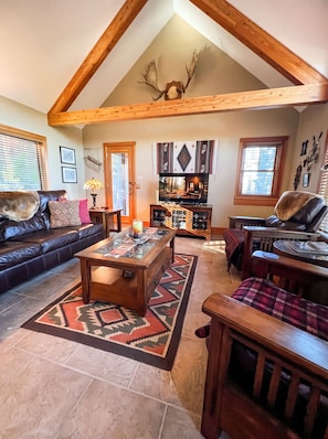 A spacious living room with a high ceiling, a fireplace, a television, and a cozy seating area. - Spectacular Views of Swan Mountain Range~Spacious Home~Perfect for Entertaining (Seeley Lake)