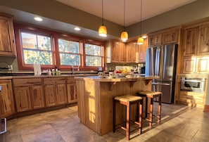 A kitchen with wooden cabinets, a stainless steel refrigerator, and a large island with stools. - Spectacular Views of Swan Mountain Range~Spacious Home~Perfect for Entertaining (Seeley Lake)