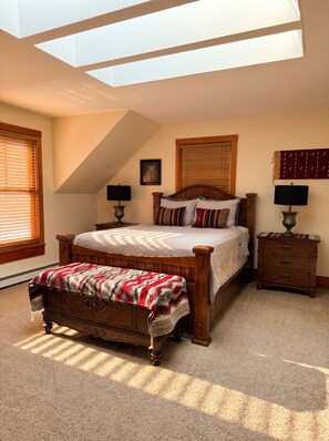 A bedroom with a skylight, a bed with patterned bedding, a bench, two bedside tables with lamps, and a wooden headboard. - Swan Mountain Views~Private 27-Acre Retreat Near Seeley Lake (Seeley Lake)