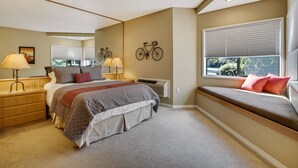 Un dormitorio con cama, lámparas de noche, un rincón ventana con cojines, un adorno de bicicleta montado en la pared y un radiador.