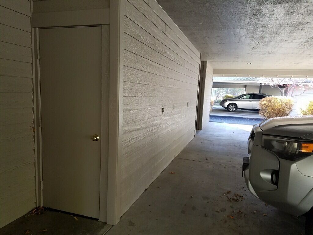 A garage with a white door, a concrete floor, and a parked car.
