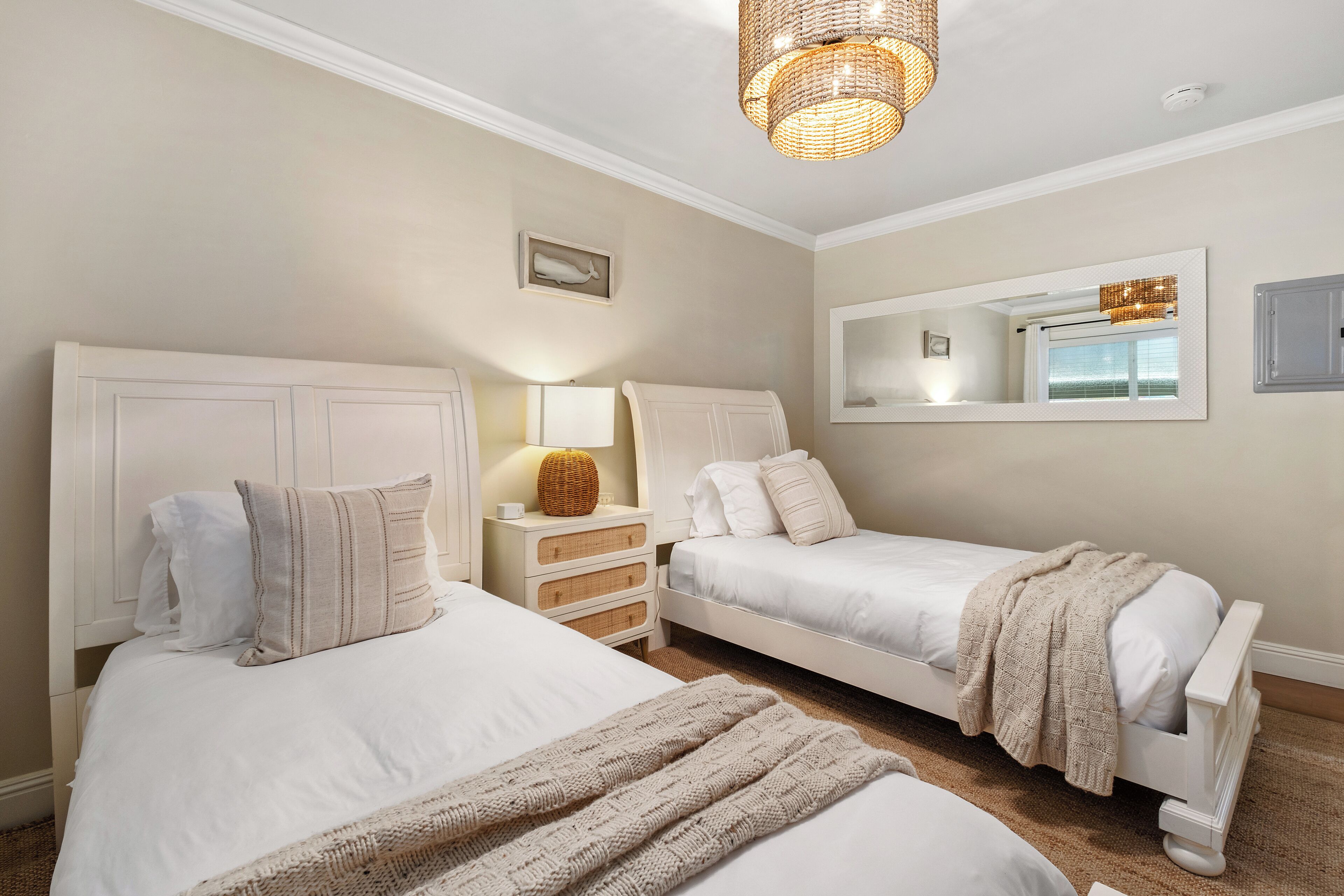 Een slaapkamer met twee bedden, een nachtkastje, een lamp, een spiegel en een plafondlamp.