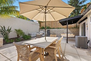 A patio with a table and chairs, a large umbrella, and a hanging chair. - Stylish Chic Hotel-style Beach Cottage-Central AC,Patio,Bikes,Walk to Beach (Capistrano Beach)