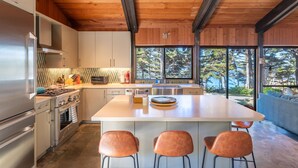 A modern kitchen with a large island, stainless steel appliances, and a view of the forest through large windows. - Pebble Beach perfection. Peaceful, Ocean view property to rest, golf, reset. (Del Monte Forest)