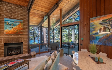 A modern living room with a fireplace, large windows, and a dining area.