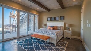 A bedroom with a large bed, a bench, a nightstand, and a view of the outside.