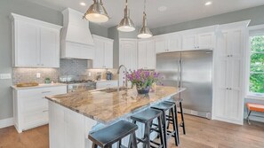 A modern kitchen with white cabinetry, a large island with bar stools, stainless steel appliances, and pendant lighting.