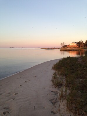 A beach with footprints leading to the water, a distant shoreline, and a house with a deck.