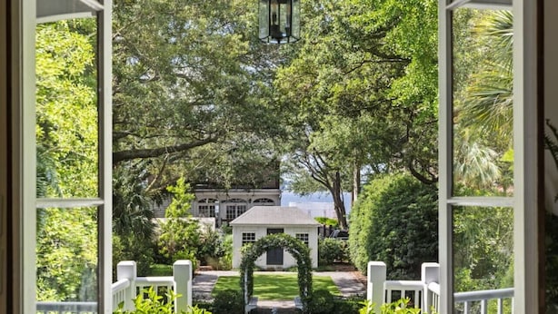 A view from a porch with two potted plants, a statue, and a well-maintained garden leading to a house. - True Southern Historic Charm by the Battery with Enchanting Charleston Gardens (Charleston)