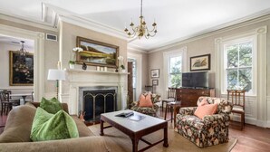 A traditional living room with a fireplace, a television, and floral-patterned furniture. - True Southern Historic Charm by the Battery with Enchanting Charleston Gardens (Charleston)