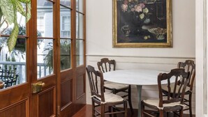 A dining area with a wooden table and chairs, a large window with a view, and a framed painting on the wall. - True Southern Historic Charm by the Battery with Enchanting Charleston Gardens (Charleston)