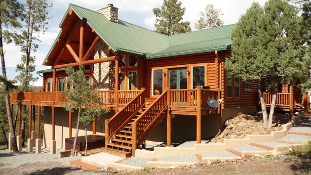A log cabin with a green metal roof, wooden deck, and a staircase leading to the entrance. - Premium Mountain Retreat On Over 2 Acres With Sweeping Views-hot Tub/Pool Table (Ruidoso)