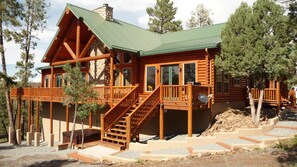 A log cabin with a green metal roof, wooden deck, and a staircase leading to the entrance. - Premium Mountain Retreat On Over 2 Acres With Sweeping Views-hot Tub/Pool Table (Ruidoso)