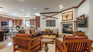 A spacious living room with a fireplace, wooden furniture, and a kitchen in the background. - Refined Rustic Retreat | Walk to Canyon Lodge, Hot Tub, Sauna & Garage (Mammoth Lakes)