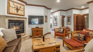 A living room with a fireplace, wooden furniture, and a mounted television. - Refined Rustic Retreat | Walk to Canyon Lodge, Hot Tub, Sauna & Garage (Mammoth Lakes)