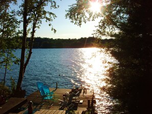 A wooden deck with chairs and a table overlooking a calm lake, surrounded by trees. - Spacious Newer Modern Home (Belgrade)