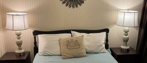 A neatly made bed with a floral quilt, two bedside lamps, a decorative mirror, and a pillow with a crest.