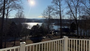 A lakeside view from a deck with a white railing, a house in the background, and a clear sky.