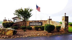 A welcome sign for Deerfield with an American flag, stone walls, and a paved road.
