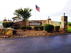 Une enseigne accueillante à l’entrée de Deerfield, avec un drapeau américain, des murs en pierre et une route asphaltée.