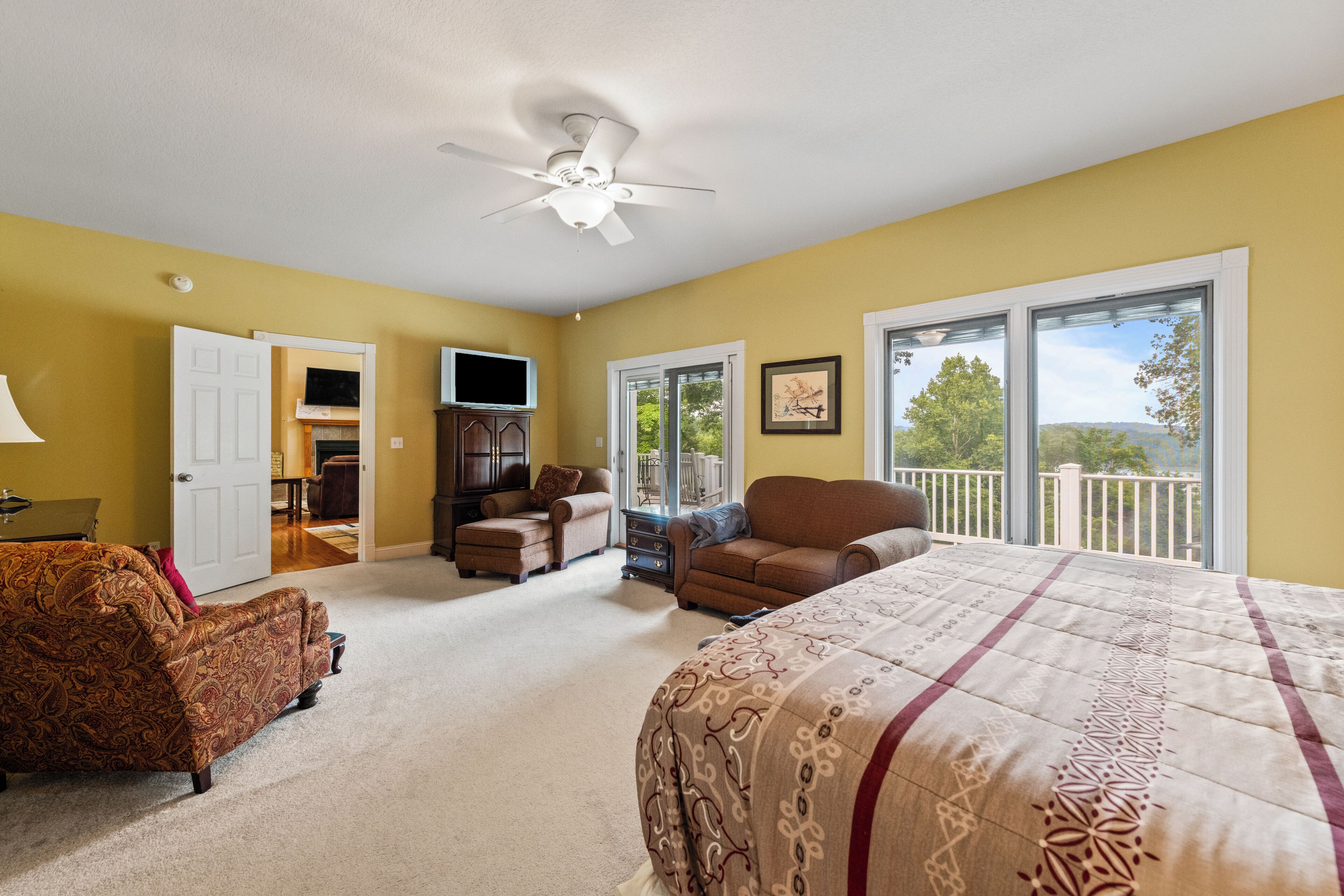 A bedroom with a bed, a chair, a television, and a balcony with a view.