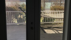 A view through a door with a window, showing a deck with a white railing and a view of trees and a distant landscape.