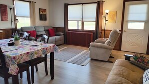 A cozy living room with a sofa, armchair, and a dining table with a floral tablecloth. - Scenic View Lodging ~ A Country Suite with Country Charm. (Gap)