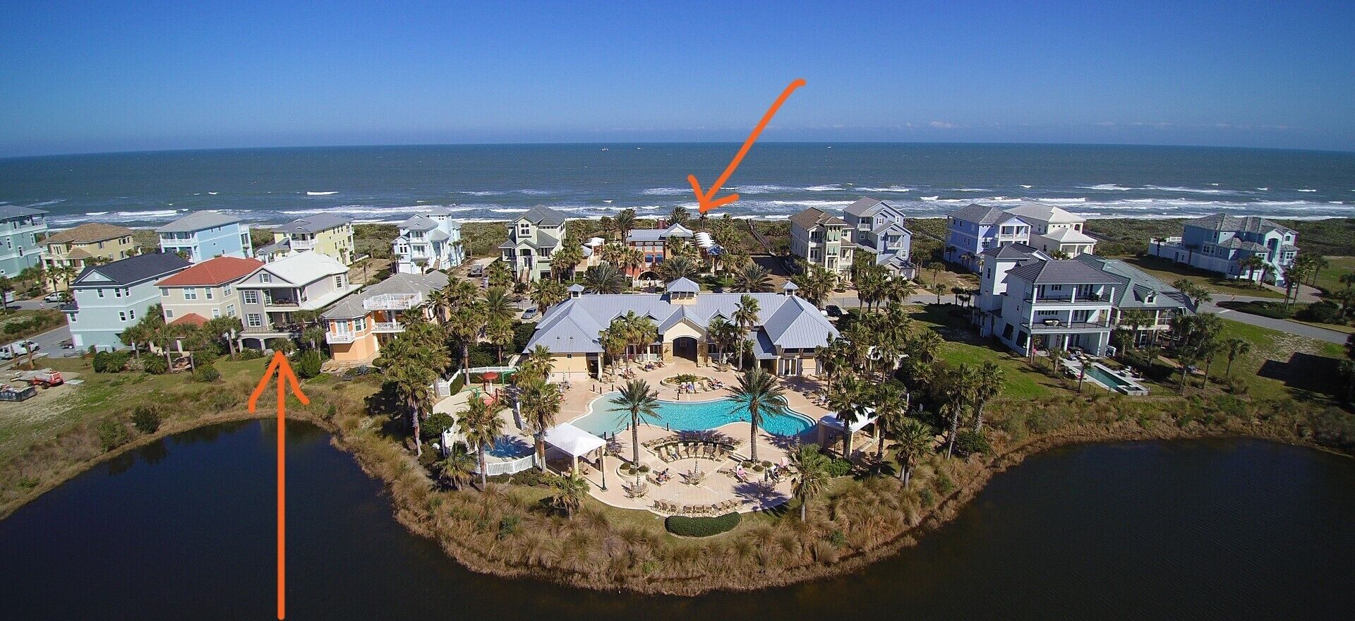 An aerial view of a coastal residential area with houses, a swimming pool, and a beach.