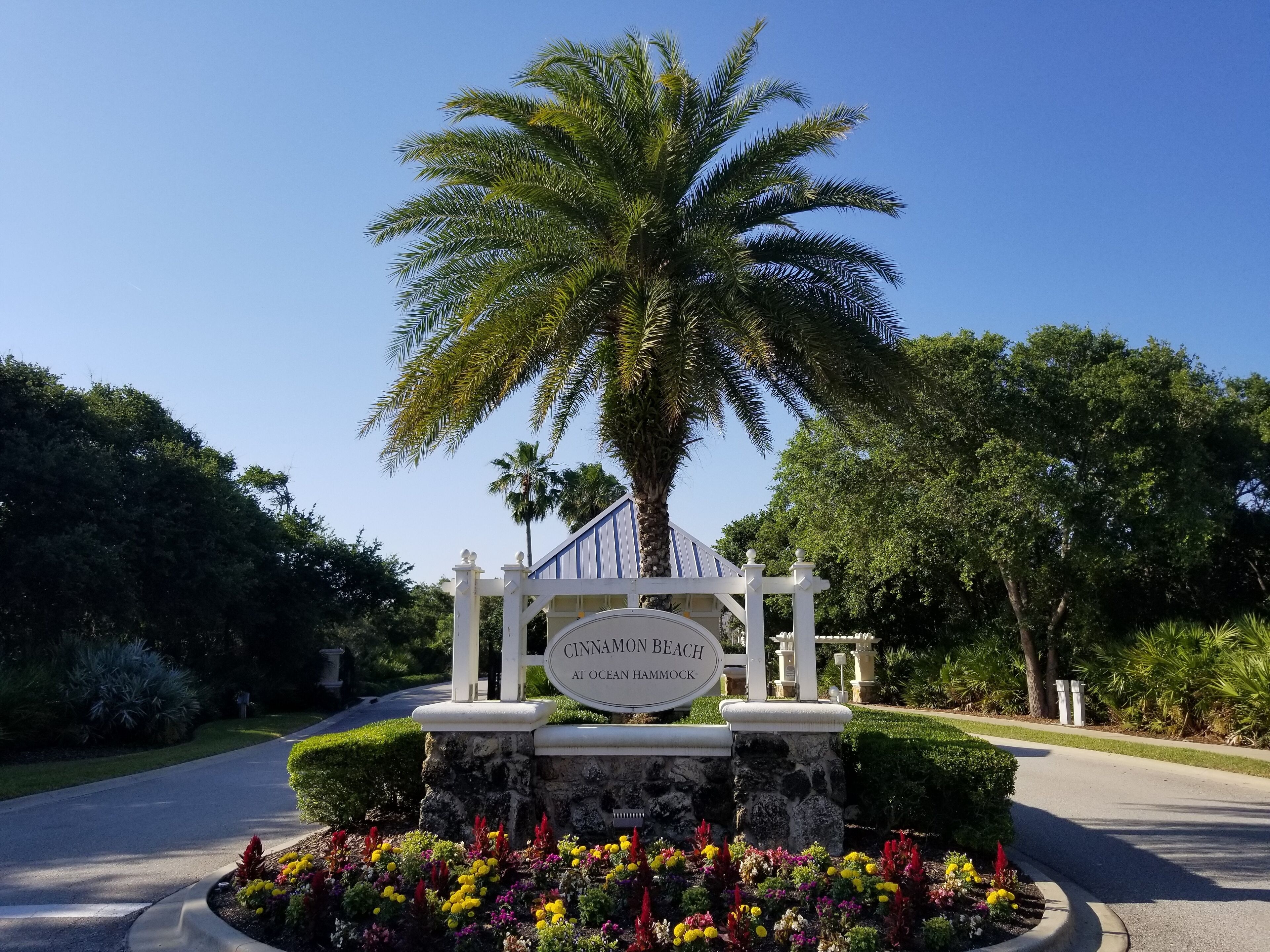 A sign for Cinnamon Beach at Ocean Hammock with a palm tree and colorful flowers in the foreground.