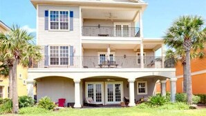 Une maison à deux étages avec un balcon au deuxième étage, un porche avant couvert et des palmiers dans le jardin.
