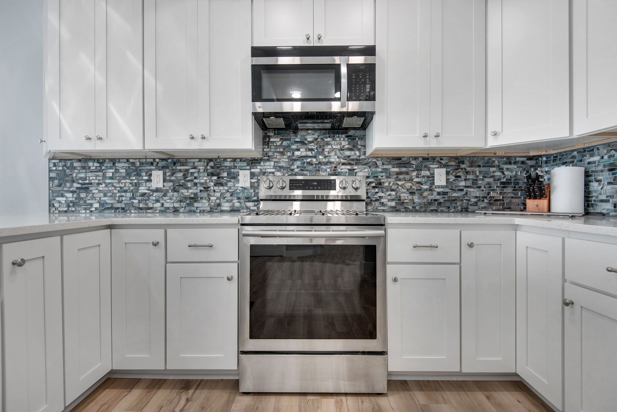 A modern kitchen with white cabinets, a stainless steel range, a microwave, and a tiled backsplash.