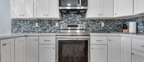 A modern kitchen with white cabinets, a stainless steel range, a microwave, and a tiled backsplash.