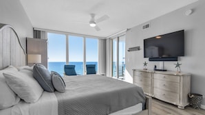 Ein Schlafzimmer mit einem großen Bett, einem Fernseher, einem Schminktisch und Blick aufs Meer.