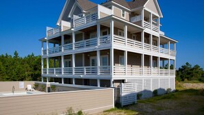 Una casa de varios pisos frente a la playa con balcones, una piscina y una playa de arena al fondo.