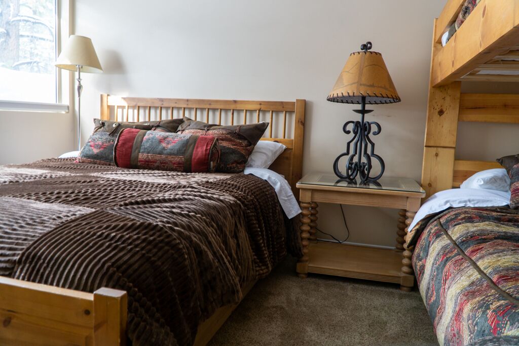 A cozy bedroom with a wooden bed, a bedside lamp, and a bunk bed.