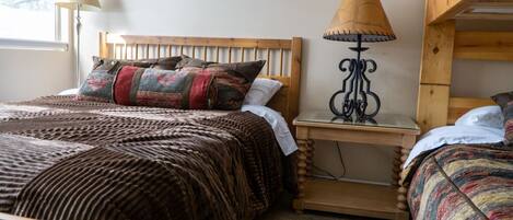 A cozy bedroom with a wooden bed, a bedside lamp, and a bunk bed.