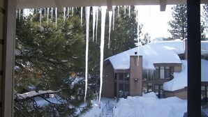 Ein überdachter Außenbereich mit von der Decke hängenden Eiszapfen, ein schneebedecktes Gebäude und eine verschneite Auffahrt.