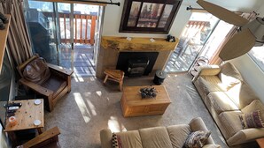 Ein gemütliches Wohnzimmer mit Kamin, Ledersofa, Couchtisch aus Holz und Blick ins Freie.