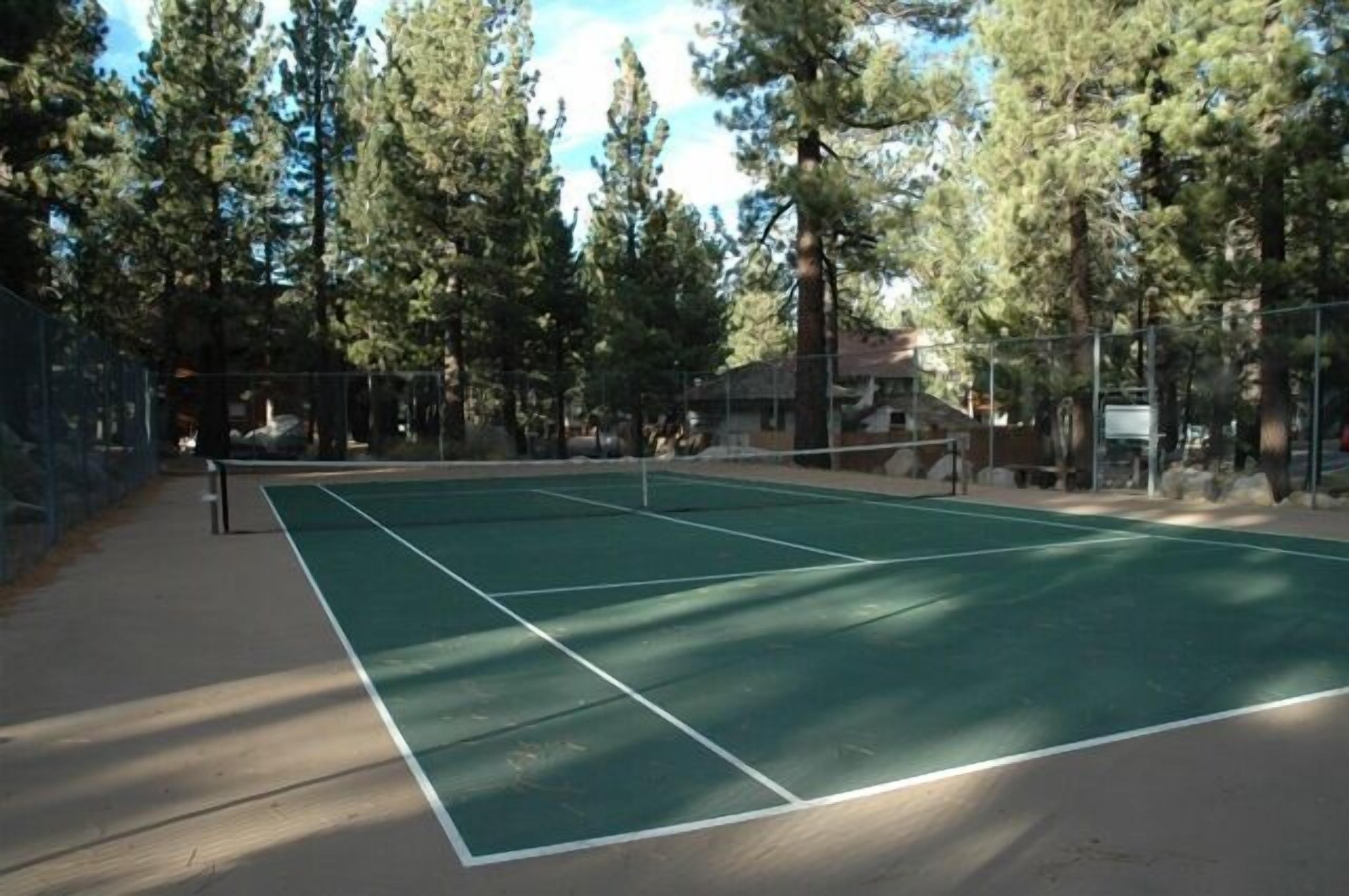 Una cancha de tenis rodeada de árboles altos y un edificio al fondo.