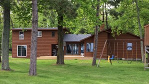 Eine Holzlaube mit Veranda, Schaukel und Rasen.