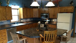 Eine Küche mit Holzschränken, einer Granit Arbeitsplatte, einer zentralen Kochinsel mit Barhocker, einem Kühlschrank, einem Backofen und einer Mikrowelle.