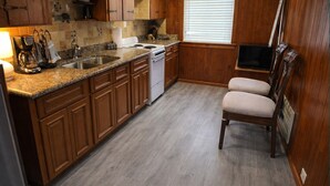 Una cocina con gabinetes de madera, encimeras de granito, estufa y lavavajillas.