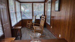Una habitación con paneles de madera, una mecedora, una mesita y un florero de vidrio.