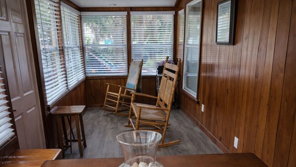 A room with wooden paneled walls, a rocking chair, a small table, and a glass vase.