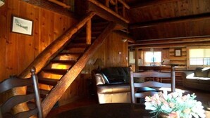Ein Holzhütten-Interieur mit Treppe, einer Couch, einem Esstisch und einem Fenster.