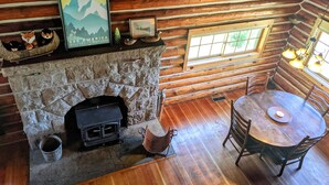 Ein Holzblockhaus-Interieur mit Kamin aus Stein, Esstisch aus Holz und Stühlen.