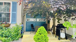 Patio trasero residencial con una parrilla y un árbol pequeño.